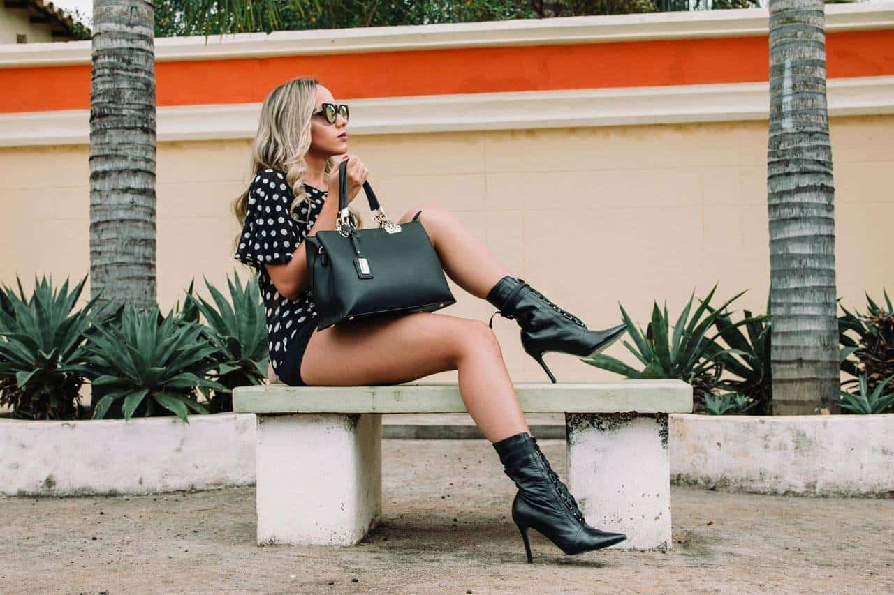 Mulher sentada em banco, moda urbana, jardim ao fundo.