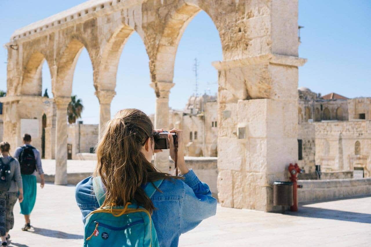 Turista fotografando ruínas históricas sob céu azul.