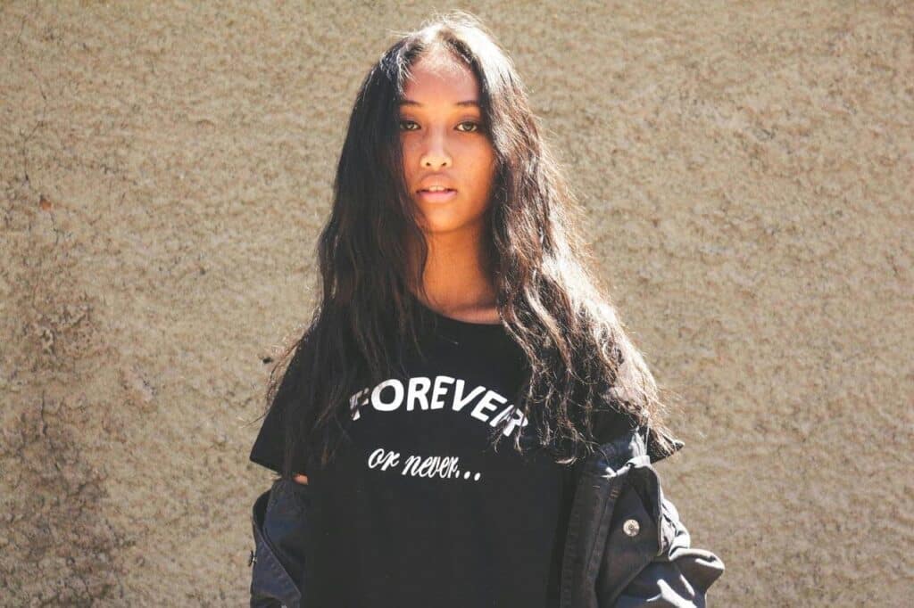 Mulher com camiseta preta, fundo de parede bege.