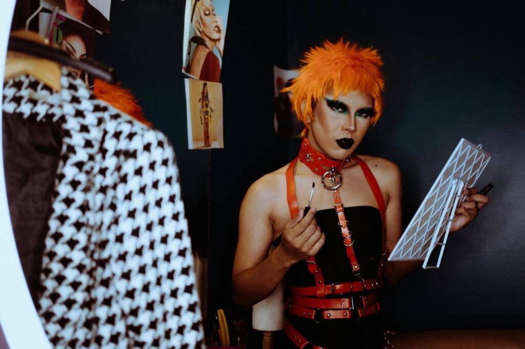 Pessoa maquiada com cabelo laranja e roupa de tiras.