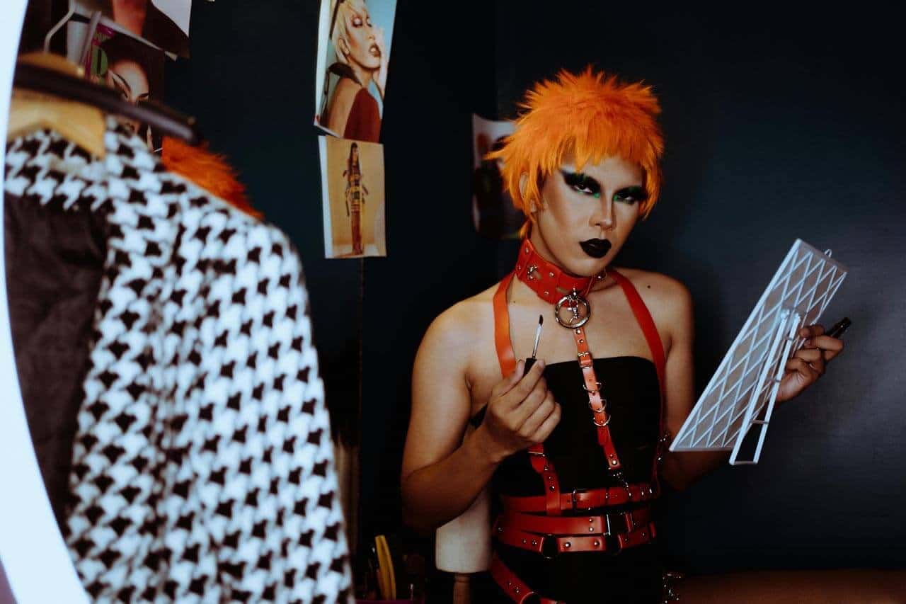 Pessoa maquiada com cabelo laranja e roupa de tiras.