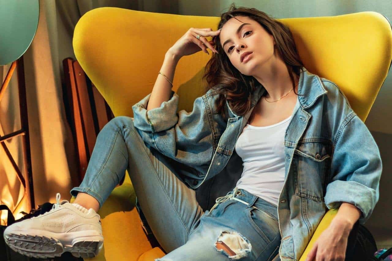 Mulher jovem em poltrona amarela com roupa jeans.