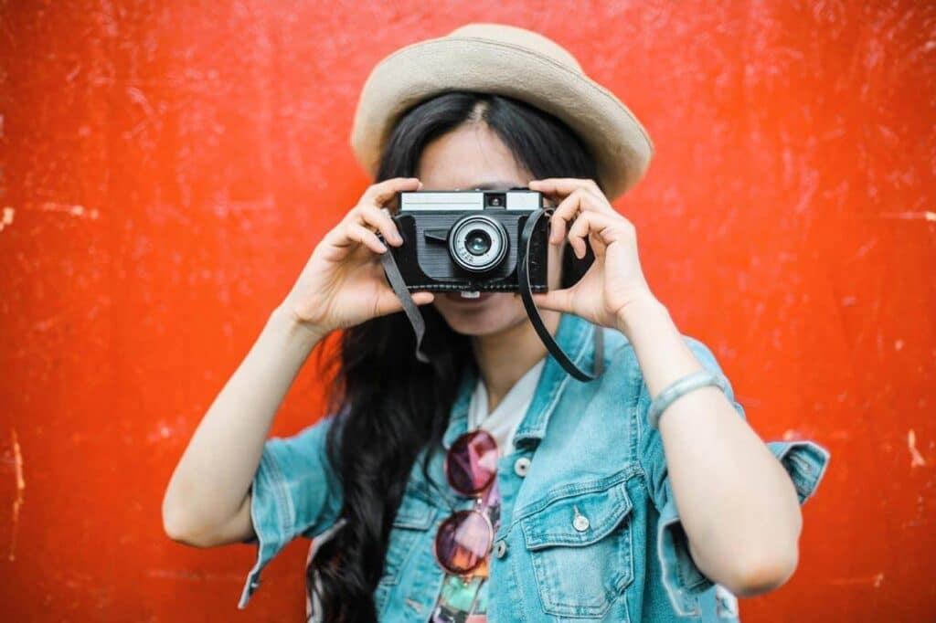 Pessoa fotografando contra parede vermelha com câmera vintage.