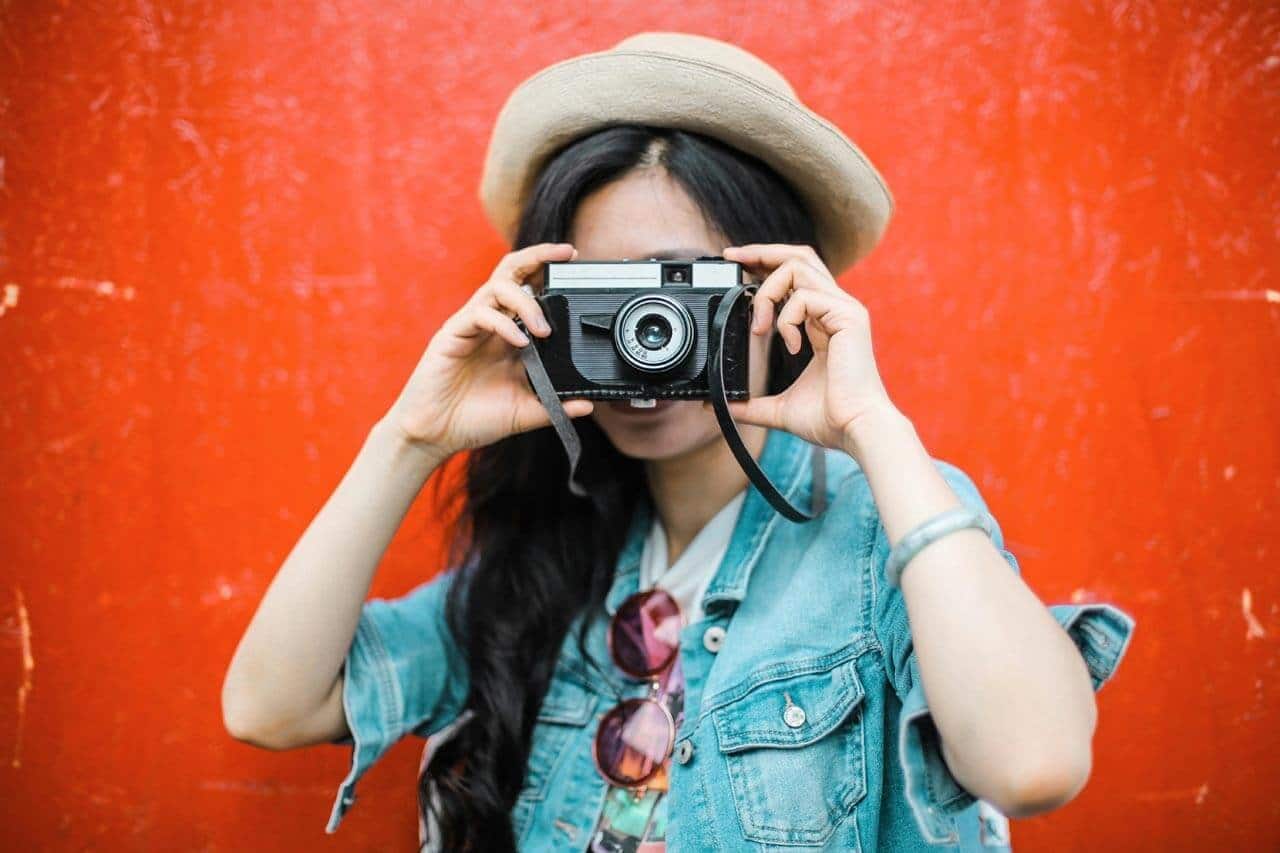 Pessoa fotografando contra parede vermelha com câmera vintage.