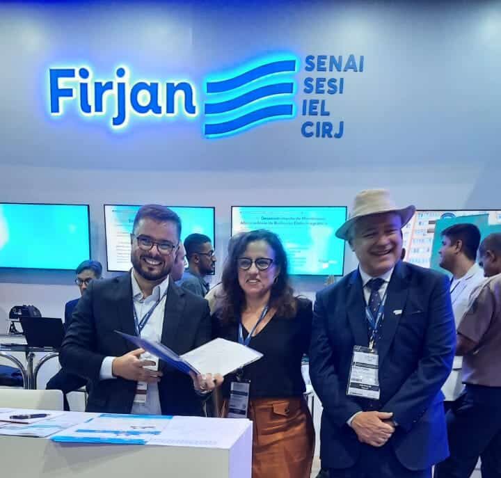 Pessoas sorrindo em estande da Firjan em evento.