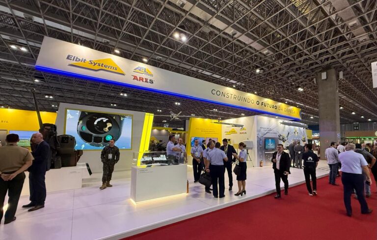 Stand de defesa em exposição industrial, pessoas interagindo.