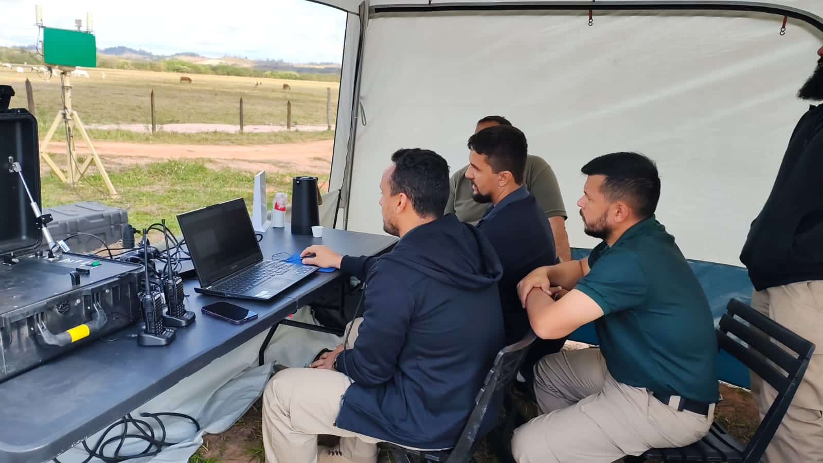 Equipe operando computadores em ambiente externo coberto.