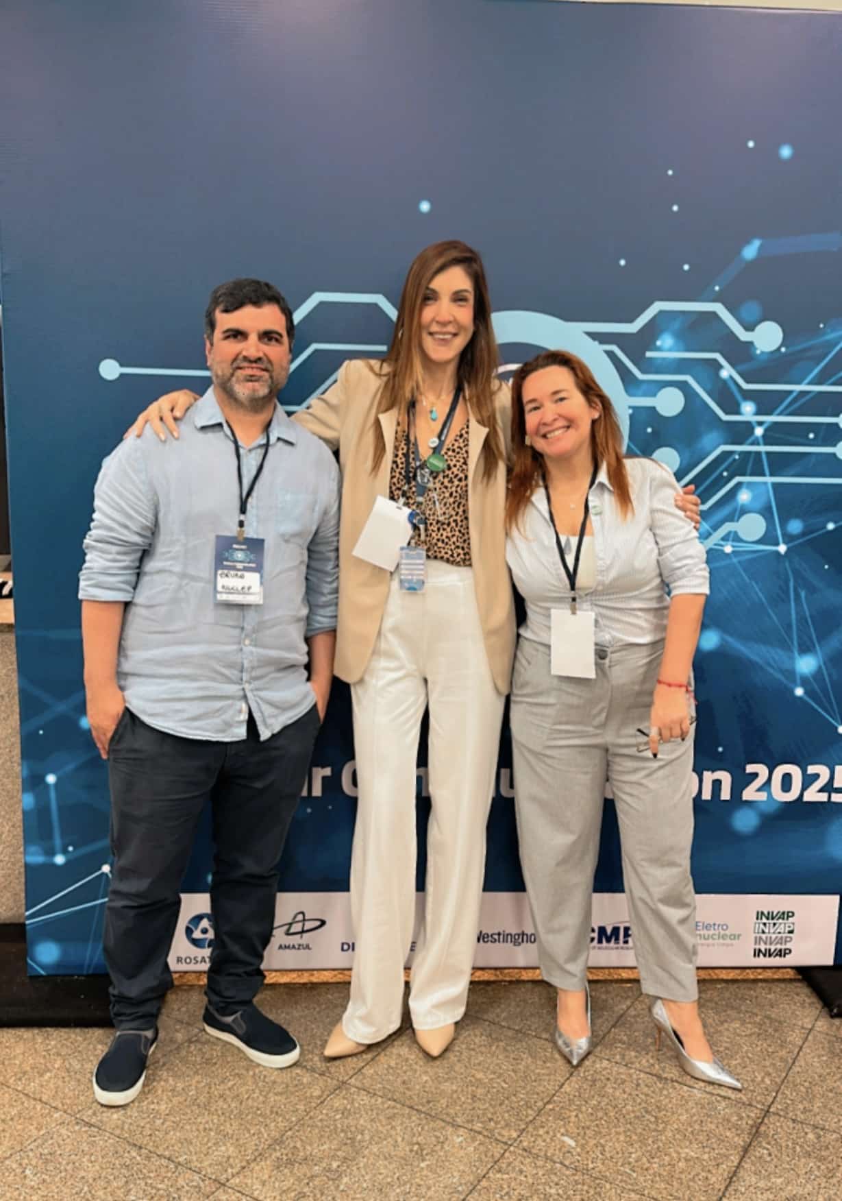 Três pessoas sorrindo em evento tecnológico.