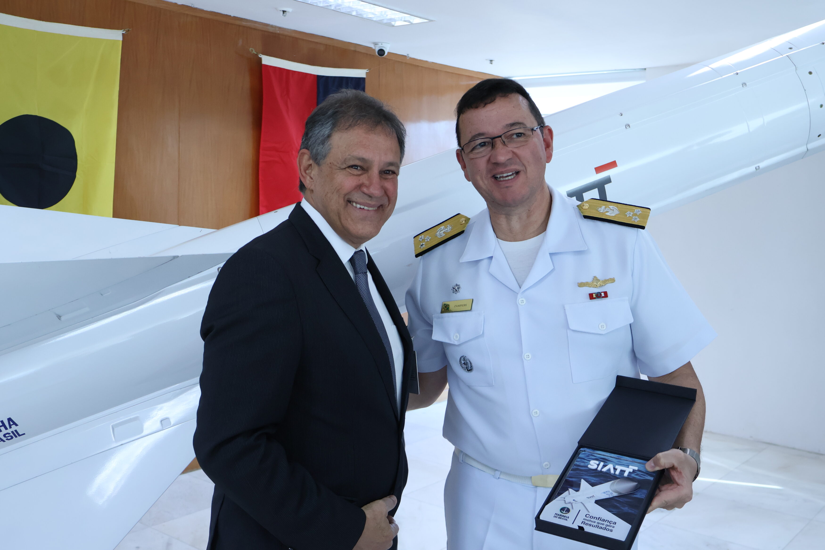 Homem de terno com militar segurando placa honorária.