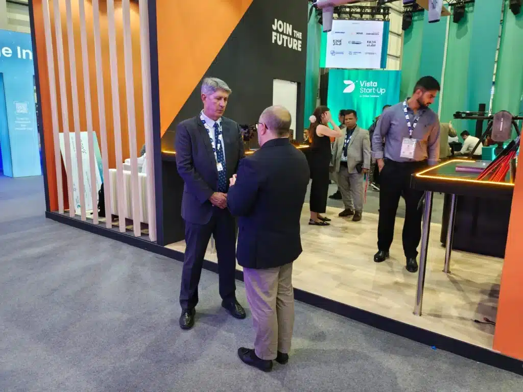 Pessoas conversam em estande de exposição tecnológica.