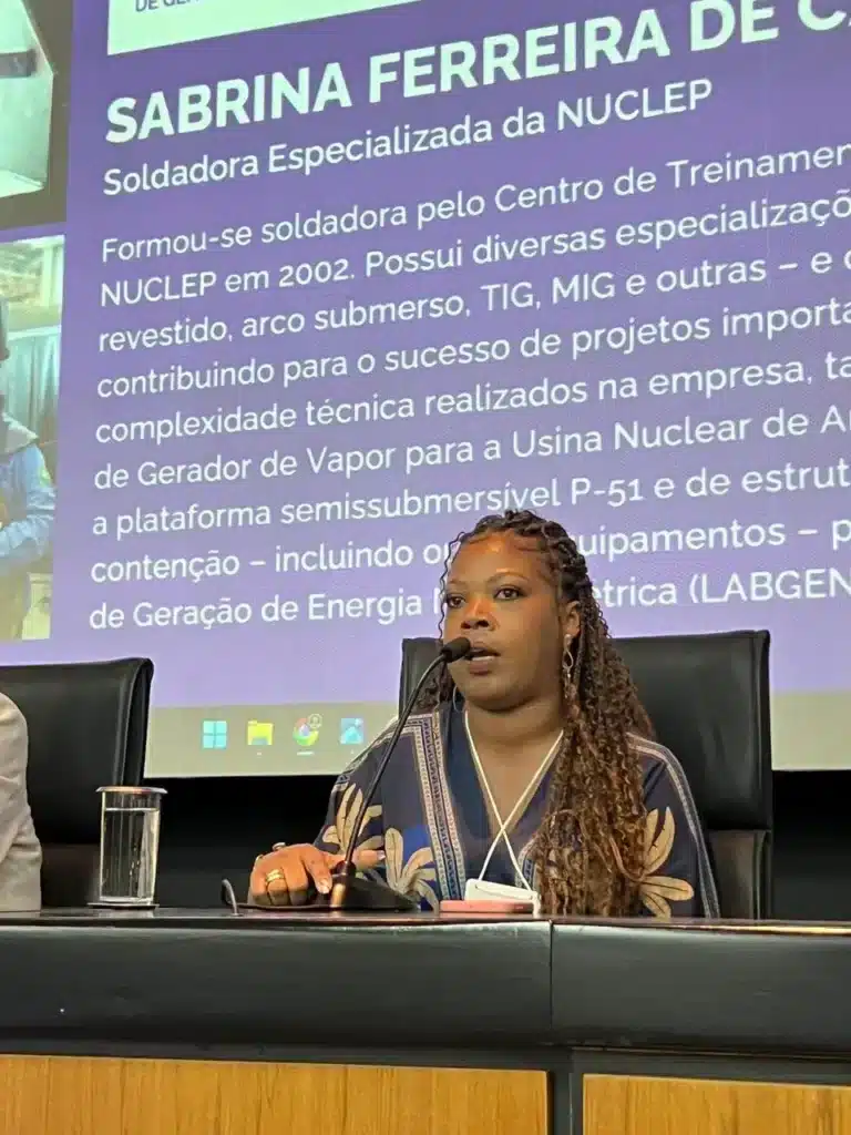 Mulher palestrante diante de tela com texto sobre soldadora.