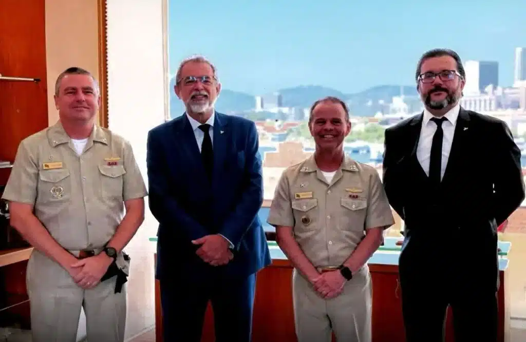 Quatro homens em pé, em frente à janela.