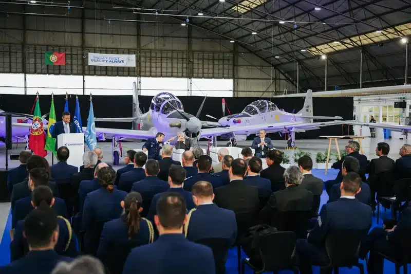 Cerimônia com aviões em hangar e público.