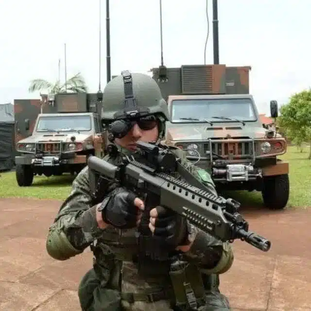 Soldado armado em frente a veículos militares.