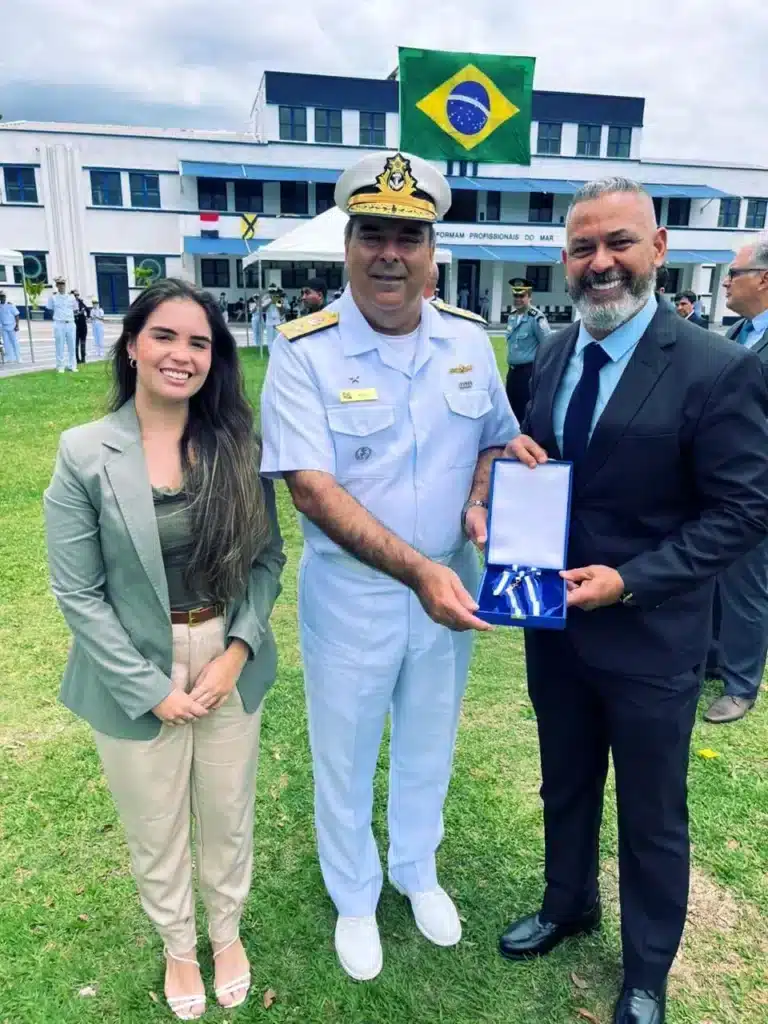 Três pessoas em cerimônia com bandeira do Brasil.