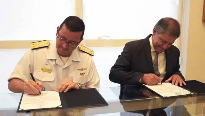 Dois homens assinando documentos em mesa.