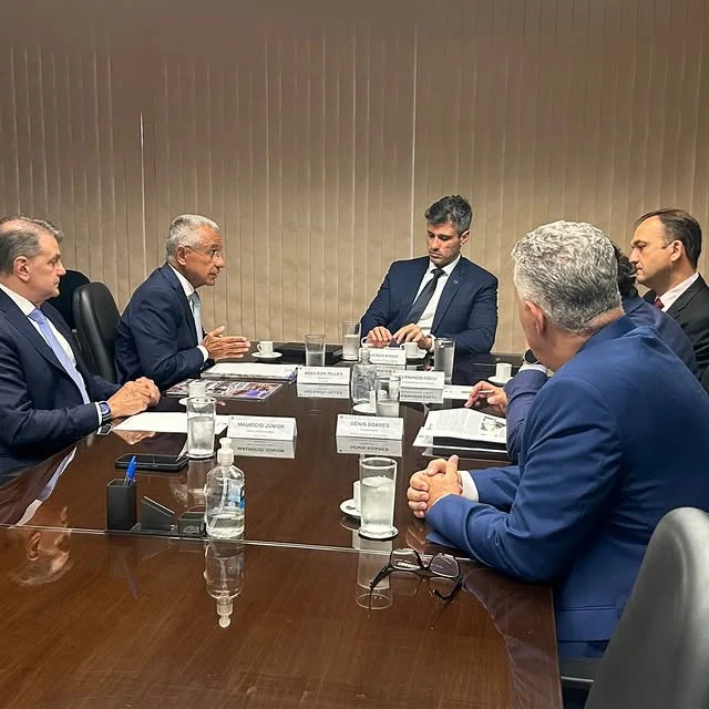 Pessoas em reunião formal ao redor de mesa.