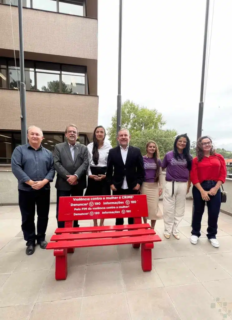 Pessoas ao redor de banco vermelho com mensagem contra violência.