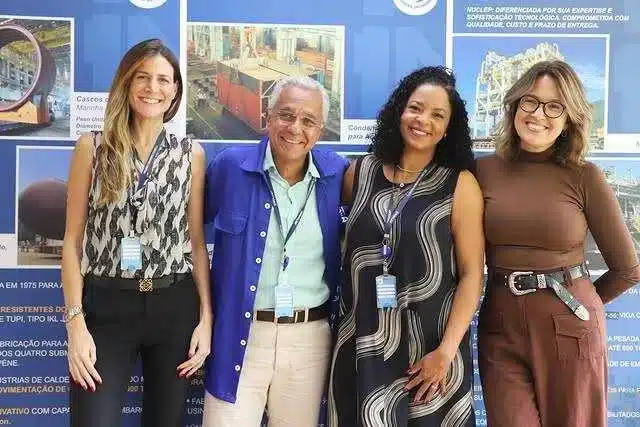 Quatro pessoas sorrindo em frente a painel azul.