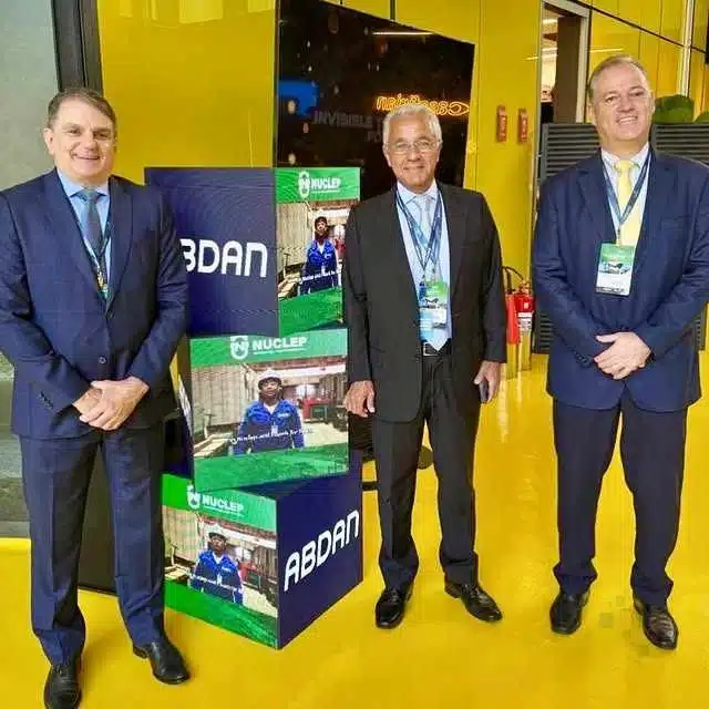 Três homens em evento corporativo, painel NUCLEN ABDAN.