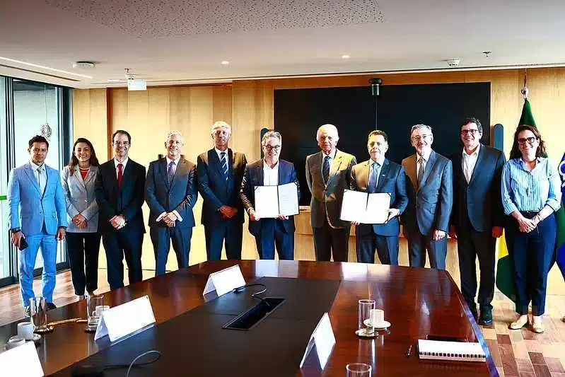 Executivos posam com documentos assinados em reunião.