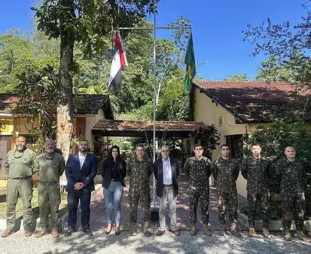 Pessoas uniformizadas posando em frente a edifício com bandeiras.
