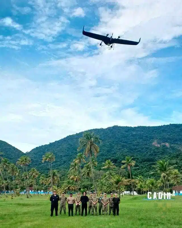 Grupo militar com drone voando em céu azul.
