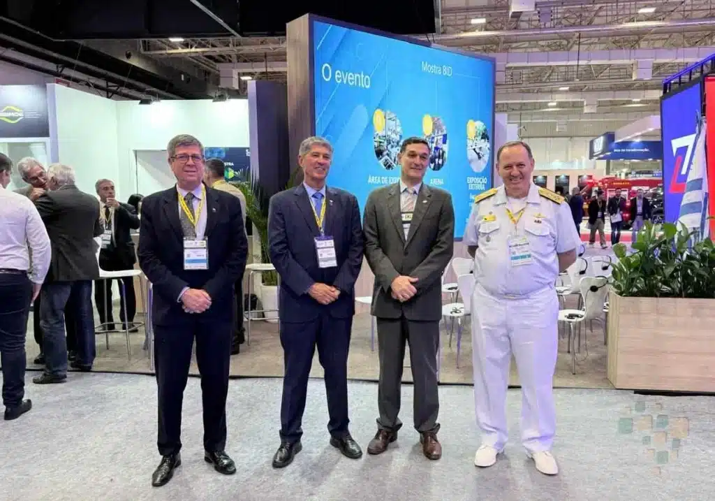 Quatro homens em traje formal em evento empresarial.