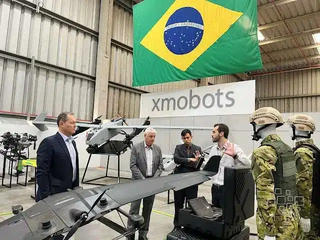 Homens discutem drones em fábrica no Brasil.