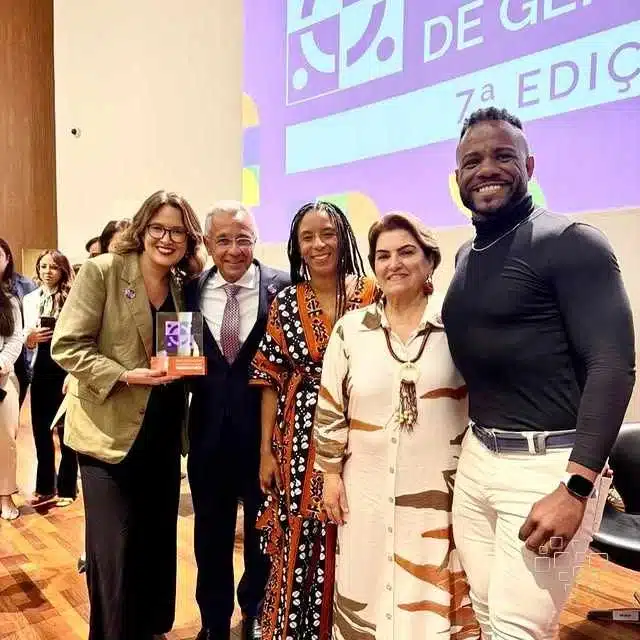 Grupo de pessoas sorrindo com troféu em evento.
