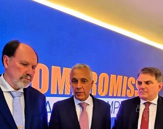 Três homens em frente a painel de compromisso.