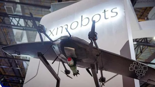 Drone em exposição com logotipo Xmobots ao fundo.