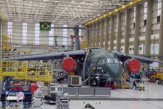 Avião militar brasileiro dentro de hangar, bandeira ao fundo.