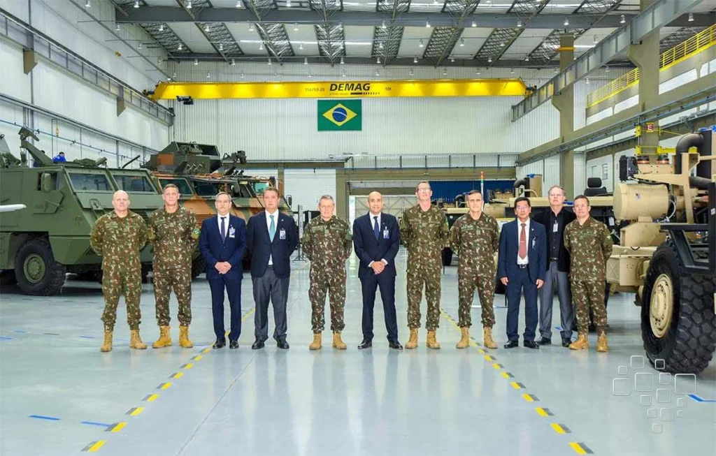 Militares e civis em hangar com veículos militares.