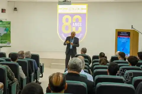 Palestrante em auditório com público atento.