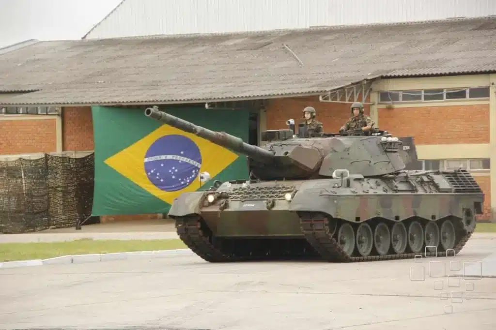 Tanque militar com bandeira do Brasil ao fundo.
