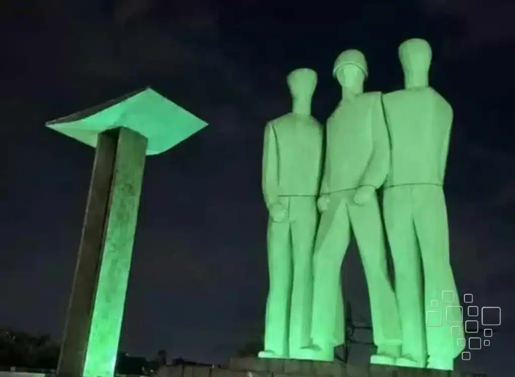 Estátua iluminada à noite com figuras humanas.