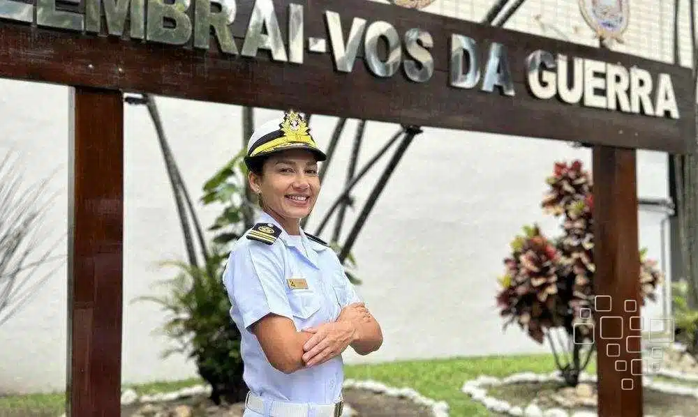 Mulher oficial naval sorrindo em frente a placa.