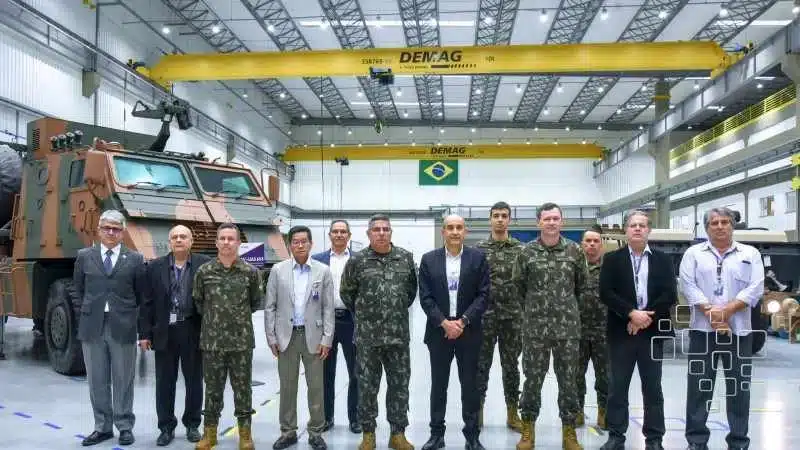 Grupo militar em frente a veículo blindado na fábrica.