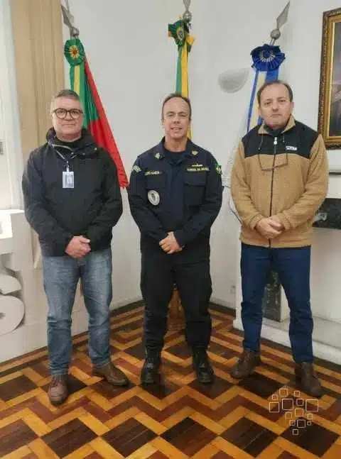 Três homens em pé em frente a bandeiras.
