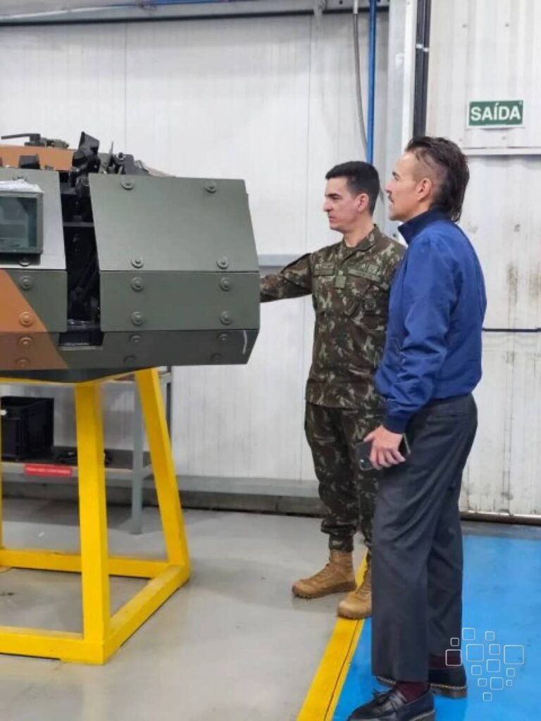 Homens observando equipamento militar em instalação industrial.