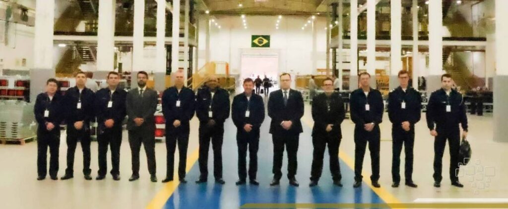 Equipe em pé em uma fábrica com bandeira brasileira.