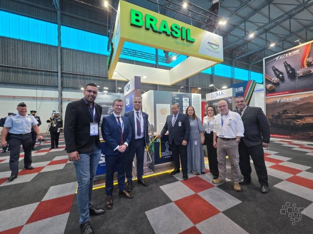 Grupo posando em frente a estande Brasil em feira.