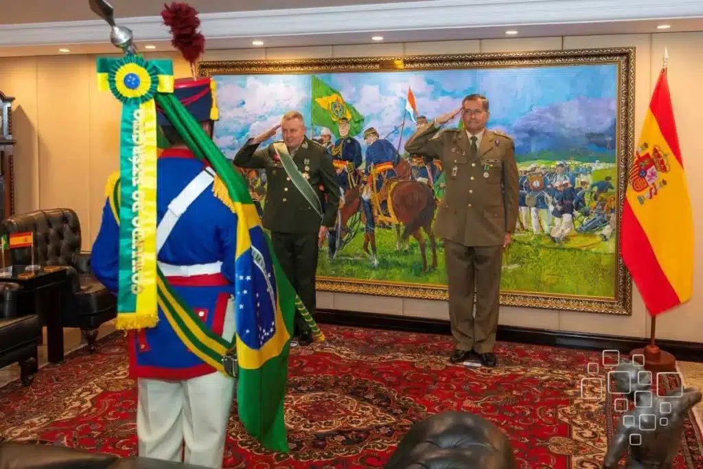Militares em cerimônia frente a bandeiras e quadro histórico.